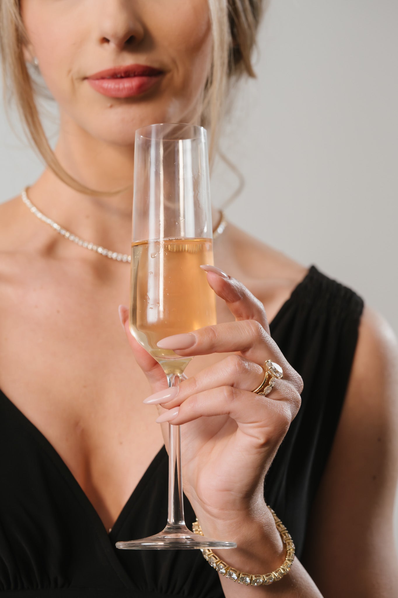 Woman holding champagne flute wearing lab-grown diamond engagement ring and bracelet