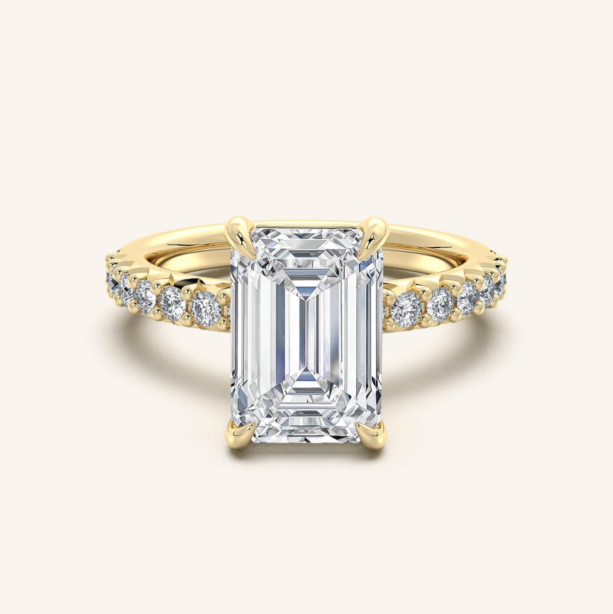 Gold ring with emerald-cut diamond and smaller diamonds on a white background
