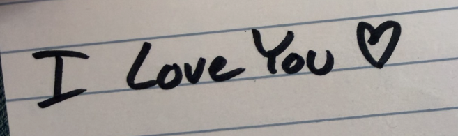 Handwritten black marker text reading 'I Love You' with a heart on lined paper.